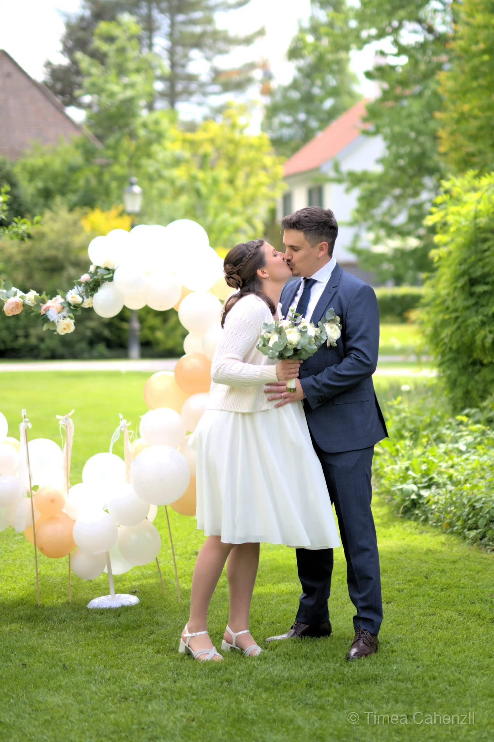 Brautpaar küsst sich vor Ballonbogen – Gartenfeier Hochzeit